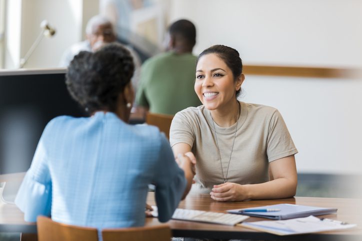 Smiling Hispanic female soldier shakes hands with a mature female bank manager.